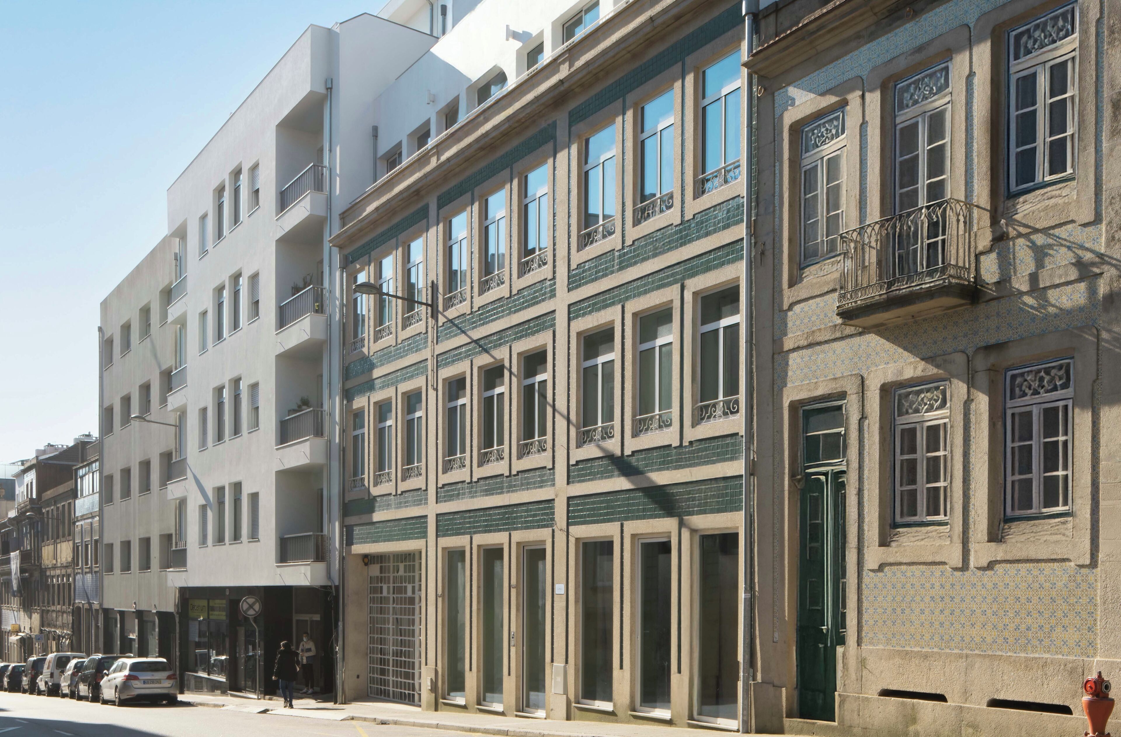 Un immeuble à plusieurs étages, avec une rangée de balcons au rez-de-chaussée, de grandes fenêtres et une porte verte.