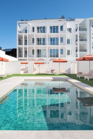 Una piscina al aire libre, sombrillas, sillones reclinables de piscina