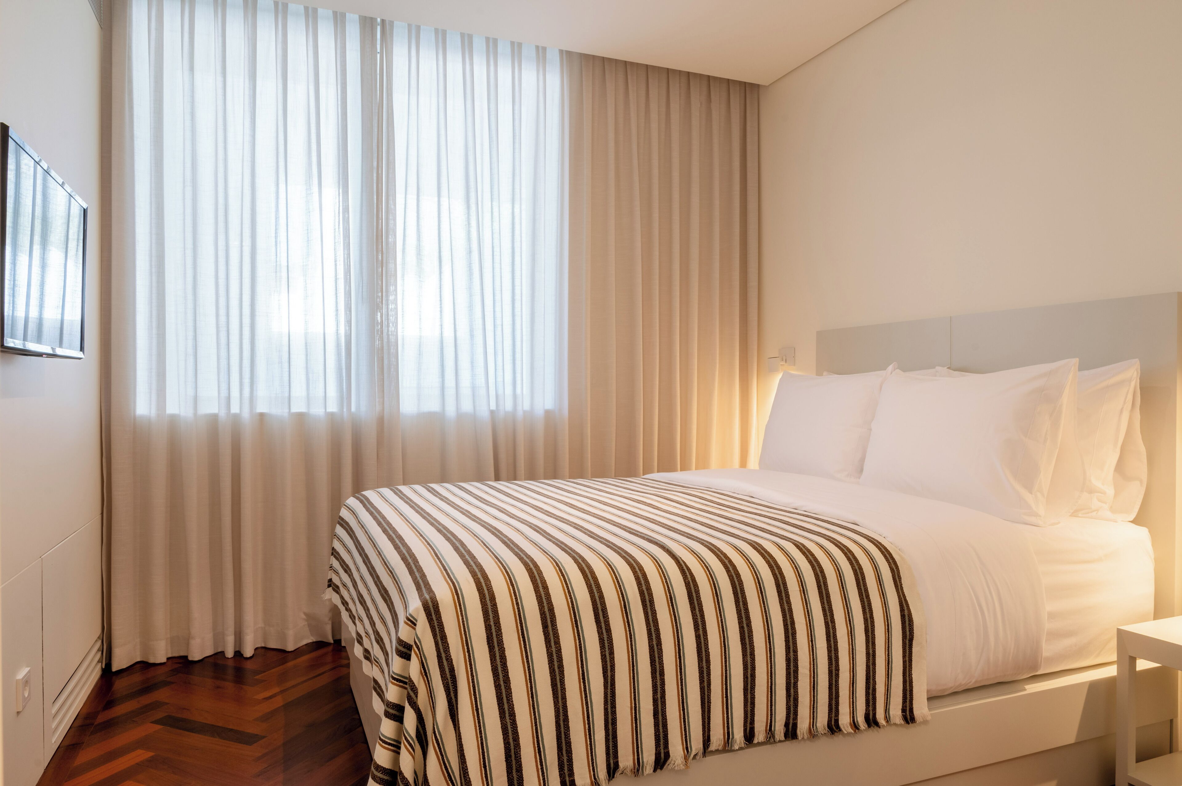 Une chambre d’hôtel avec un grand lit, des rideaux blancs et un plancher en bois.