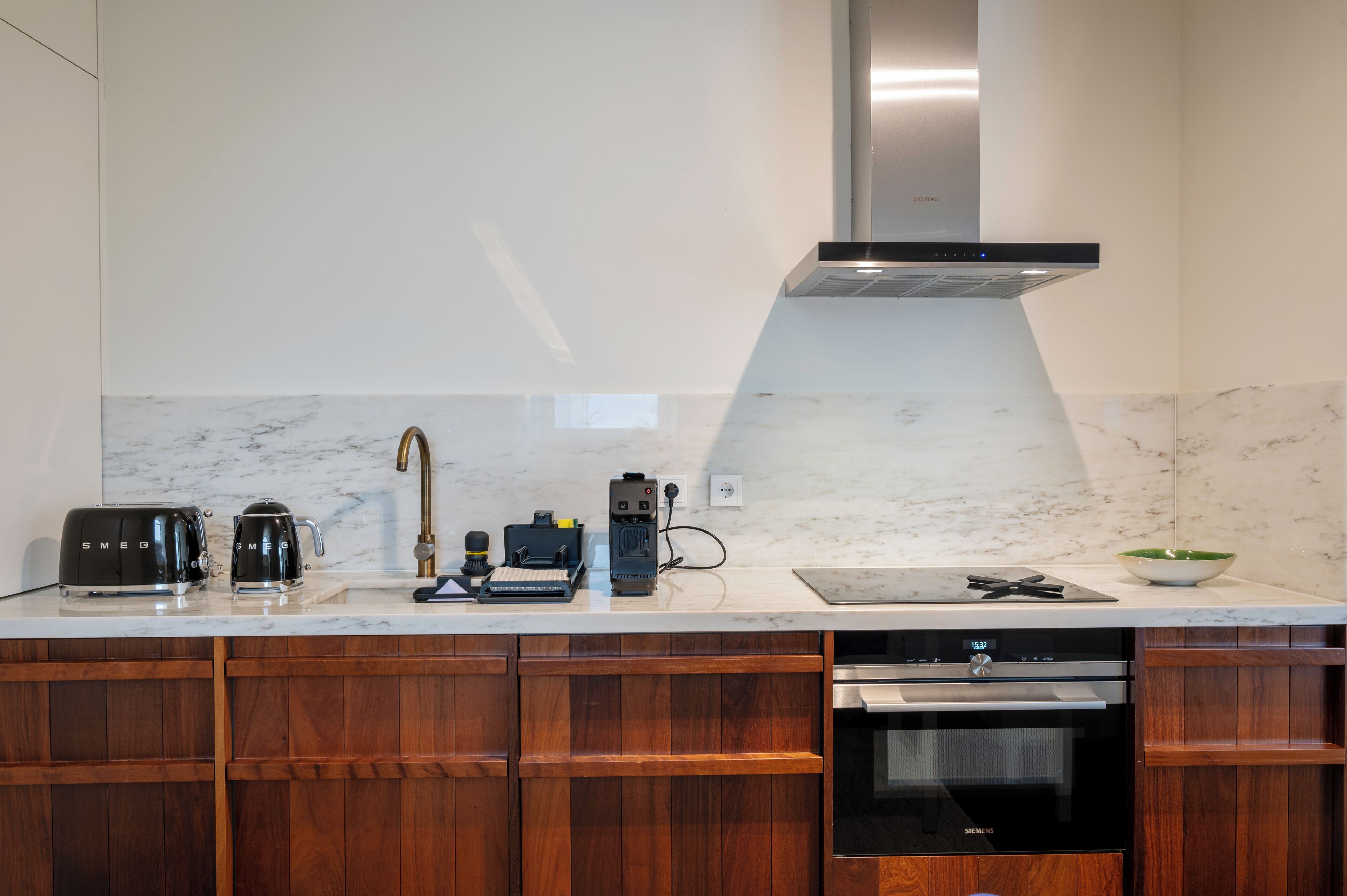 Una cocina moderna con campana de acero inoxidable, encimera de mármol, armarios de madera y horno Siemens.