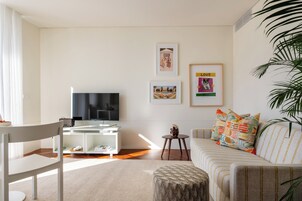 Una sala de estar con televisor, sofá, sillón, una mesita y una planta.