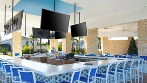 An outdoor bar area with a long counter, multiple screens, and blue and white chairs. - DLuxx Beautiful Decor House fun Waterpark 1171 (Davenport)