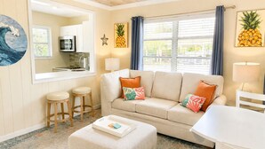 Una sala de estar acogedora con un sofá, un reposapiés y dos taburetes. Cuenta con una zona de cocina con microondas y una decoración con forma de estrella de mar.