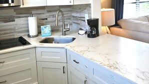 Cocina moderna con armarios blancos, un lavamanos de acero inoxidable y un microondas empotrado.