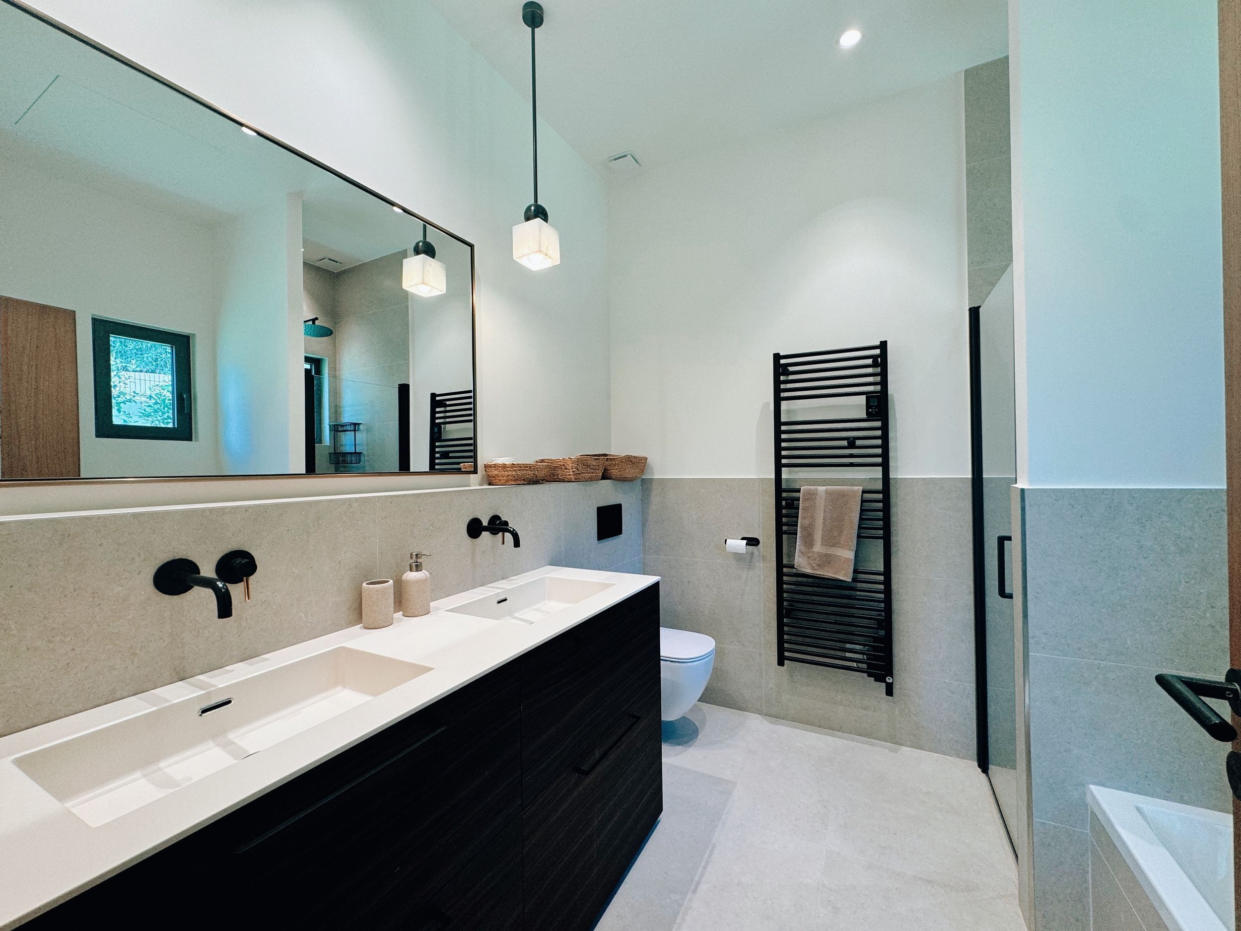 A modern bathroom with a large mirror, dual sinks, a toilet, and a towel rack.