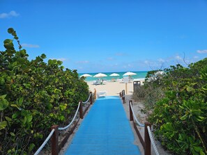 A beach pathway leading to a sandy beach with umbrellas and lounge chairs.