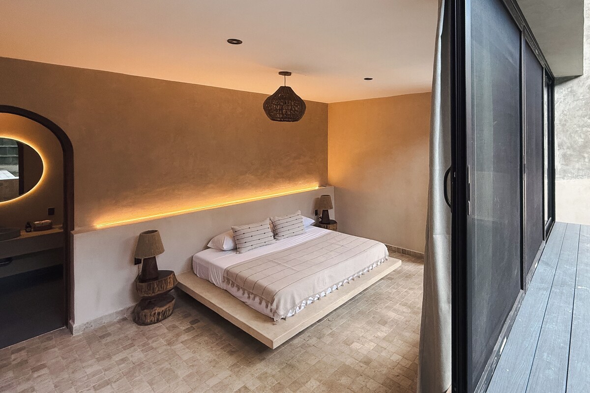 A modern bedroom with a large bed, bedside lamps, a wall-mounted light, and a view of a pool through a sliding door.