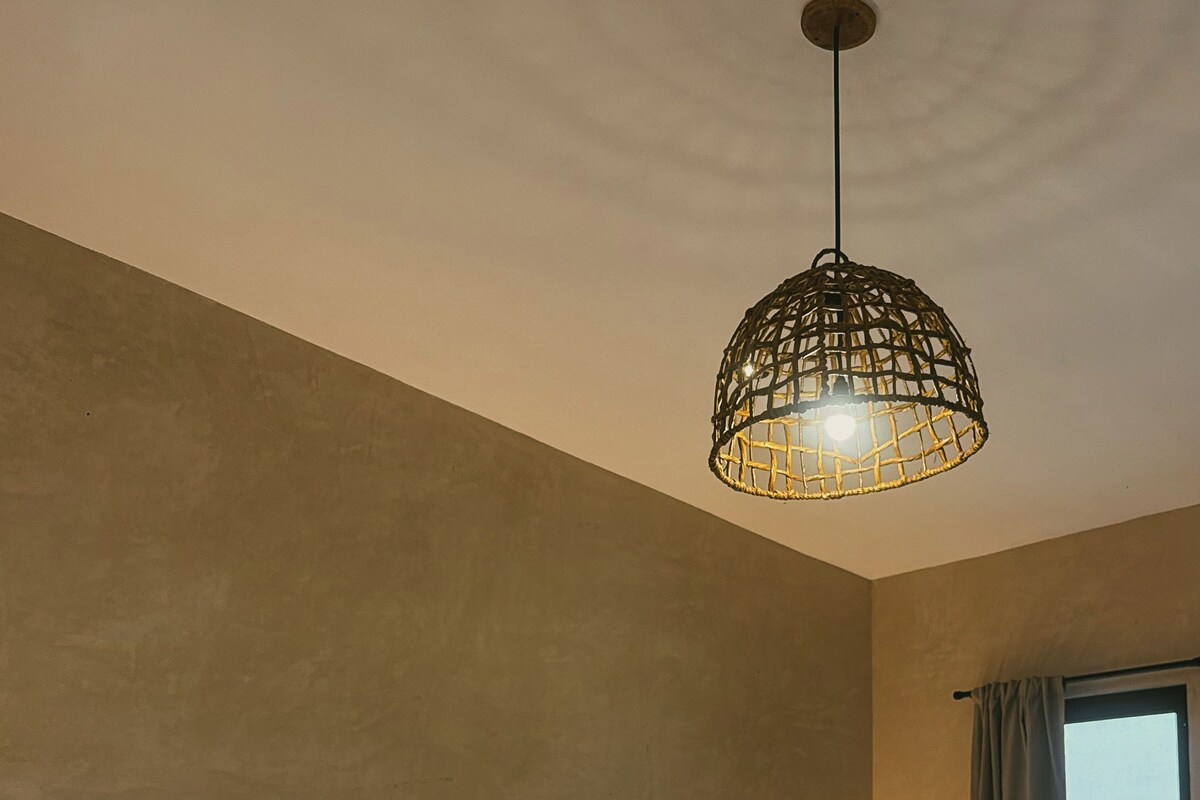 A bedroom with a bed, bedside tables, a hanging light fixture, and a window with curtains.