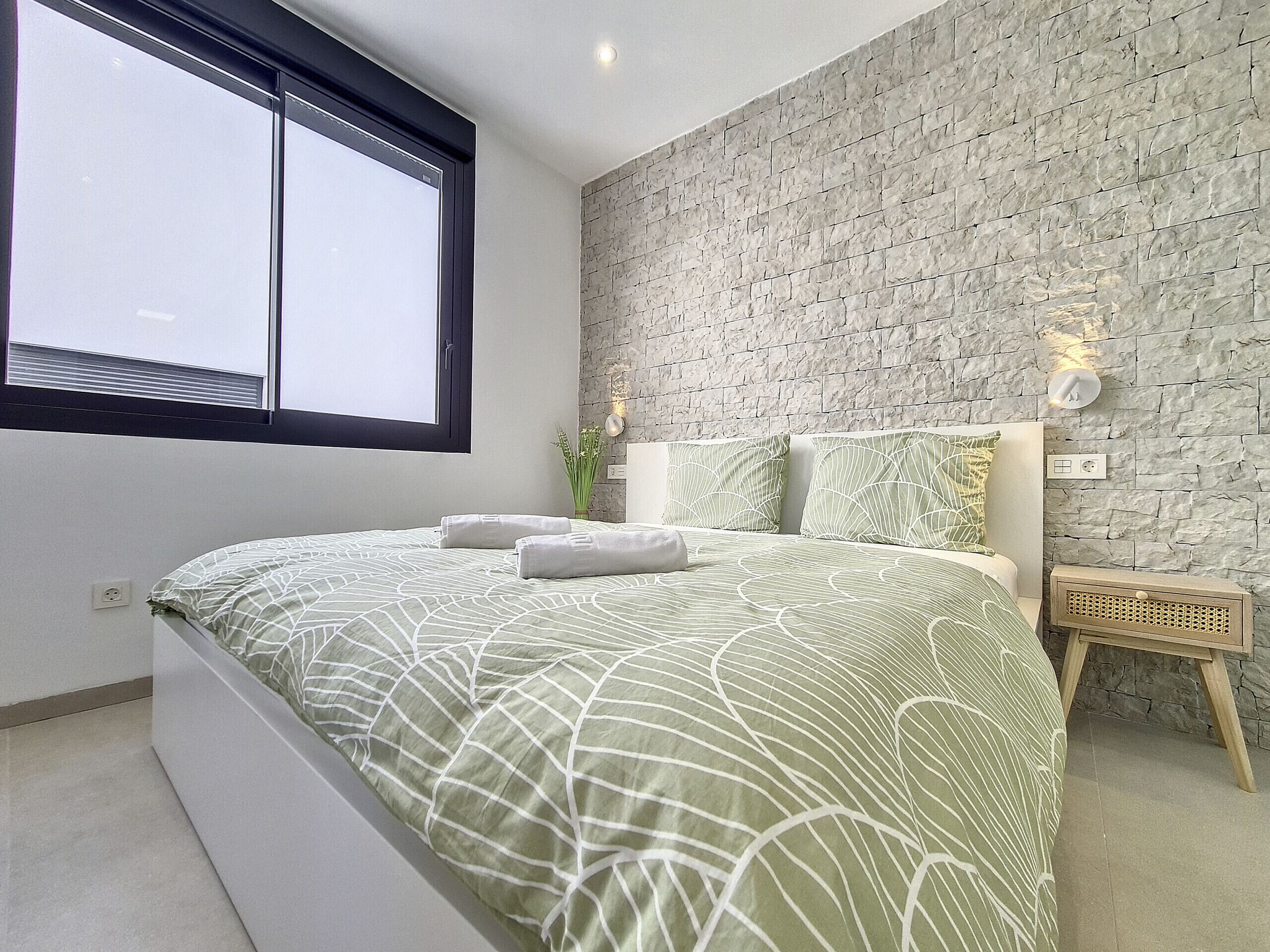 Ein Schlafzimmer mit einem großen Bett, einem Fenster, einer Steinwand und einem Nachttisch mit Lampe.