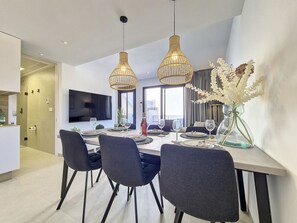 Un espace repas moderne avec une table rectangulaire, des chaises foncées et deux lampes suspendues.