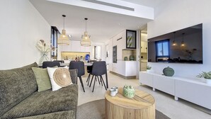 A modern living room with a sofa, a coffee table, and a dining area with chairs and a table. There is a kitchen area with a TV mounted on the wall. - Penthouse apartment with pool, parking and Wi-Fi (San Pedro del Pinatar)