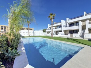A modern pool area with a clear blue pool, surrounded by well-maintained grass and palm trees. - Penthouse apartment with pool, parking and Wi-Fi (San Pedro del Pinatar)