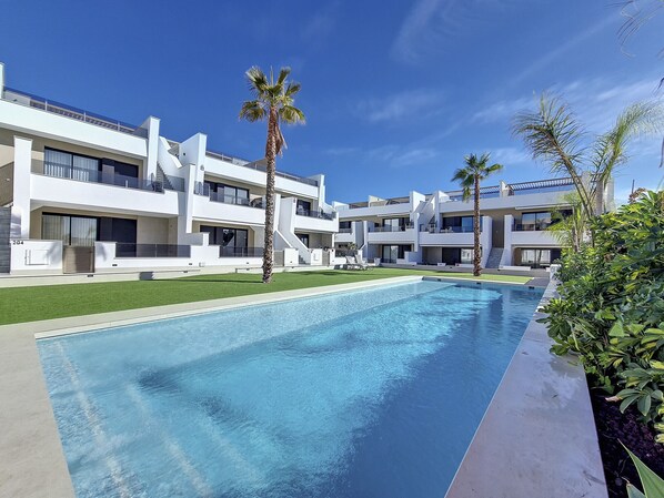 A modern residential complex with a swimming pool, palm trees, and a clear blue sky. - Penthouse apartment with pool, parking and Wi-Fi (San Pedro del Pinatar)