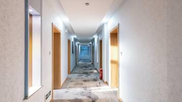En hotellkorridor med dörrar på båda sidor, ett mönstrat golv och en brandsläckare på höger sida.