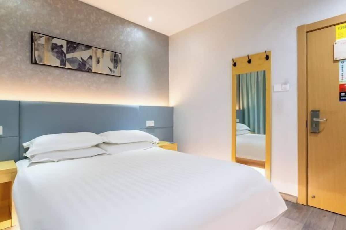 A hotel room with a large bed, a headboard, a bedside table, a mirror, and a door.