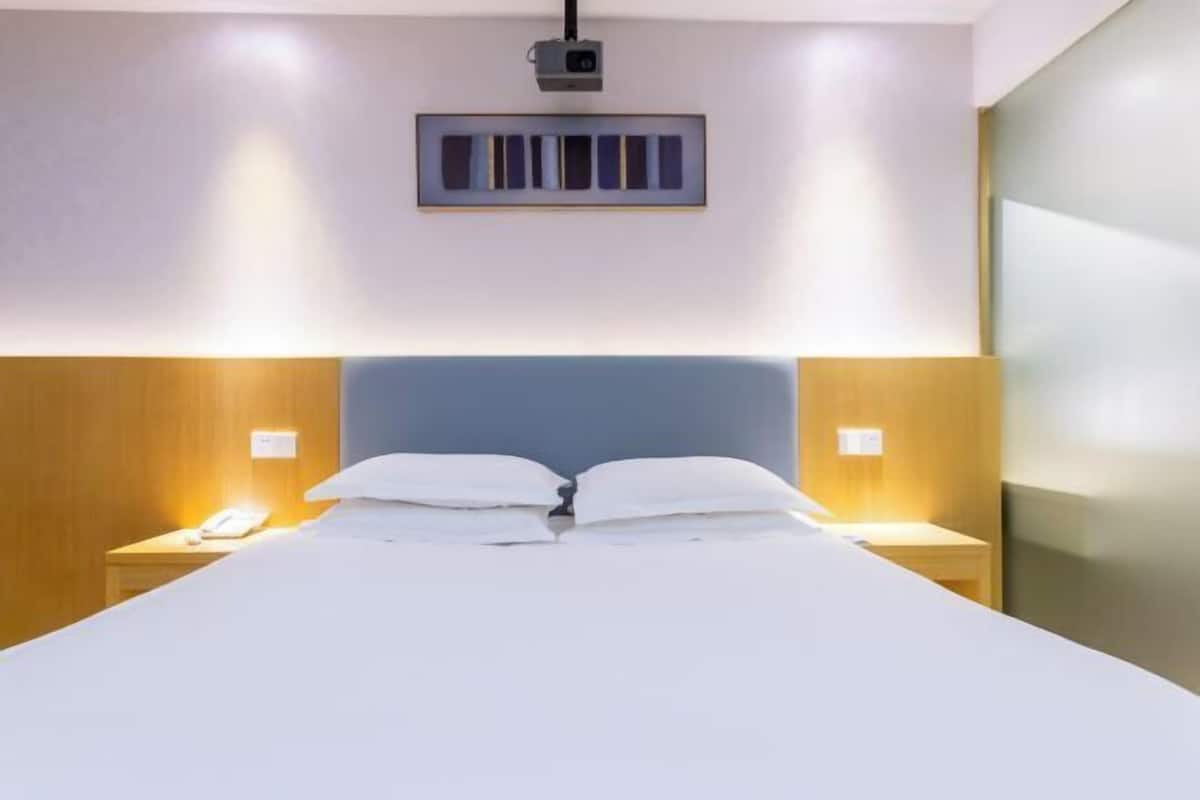 A modern hotel room with a large bed, wooden headboard, bedside lamps, and a projector mounted on the wall.