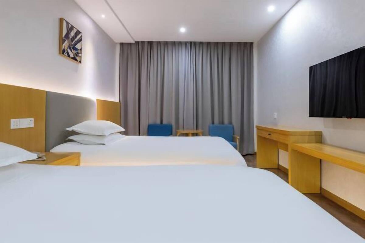 A hotel room with a large bed, a desk, a chair, and a TV mounted on the wall.