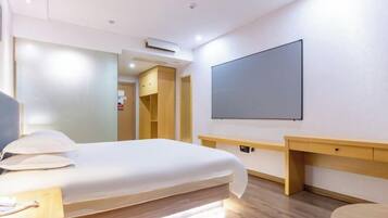 Habitación de hotel con cama, mesita de noche y televisor de pantalla plana montado en la pared.