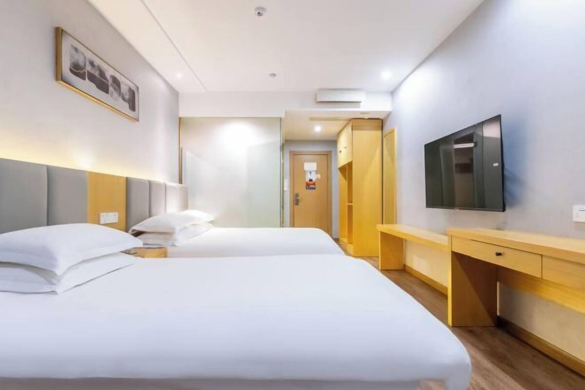 A hotel room with two beds, a desk, a TV, and a framed picture on the wall.