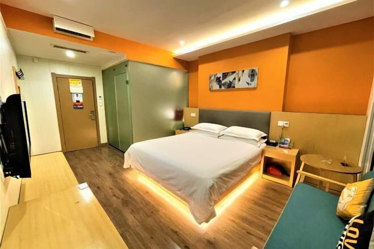 A modern hotel room with a large bed, bedside tables, a small seating area, and a door leading to another room.