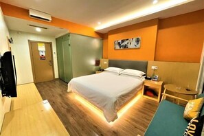 Moderni hotellihuone, jossa on suuri sänky, yöpöydät, pieni oleskelualue ja ovi, joka johtaa toiseen huoneeseen.