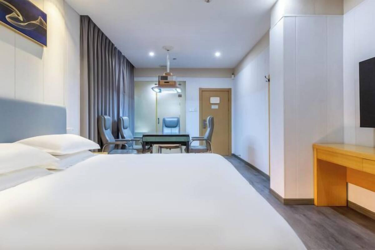 A hotel room with a large bed, a desk with two chairs, a television, and a door.