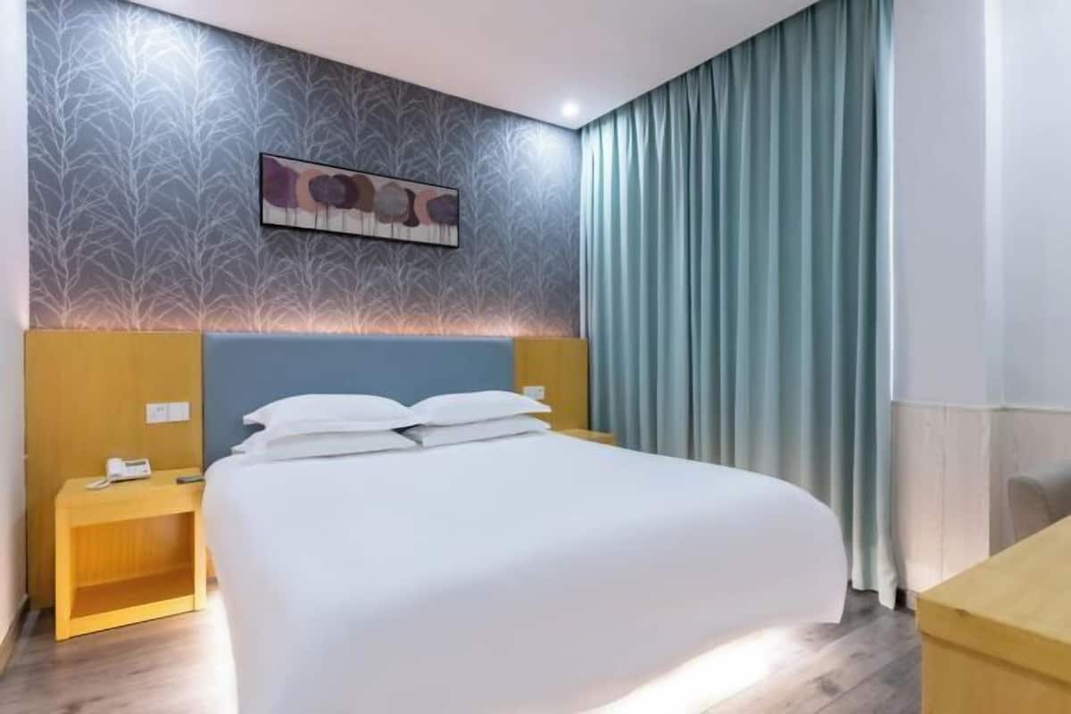 A hotel room with a bed, a nightstand, a wall-mounted artwork, and a window with curtains.