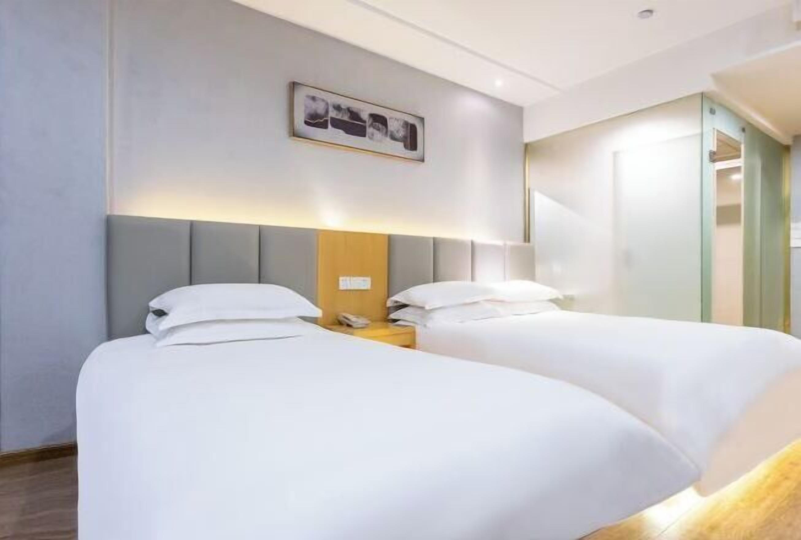 Una habitación de hotel con dos camas, una mesita de noche con lámpara y un cuadro en la pared.