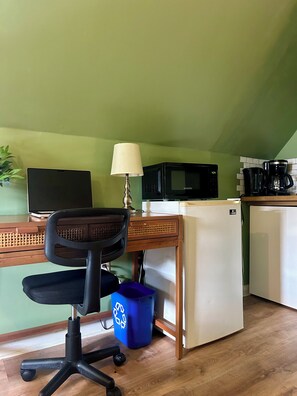 Compact kitchenette with a desk, refrigerator, microwave, coffee maker, and kettle.