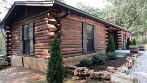 Ein Blockhaus mit Veranda, einer Flagge und einem gepflegten Garten mit Steinen und Sträuchern.