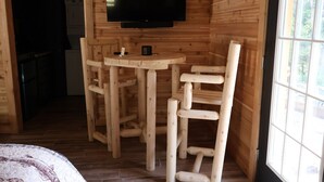 Un interior de madera con una televisión montada en la pared, una mesita y dos sillas.