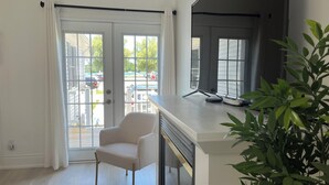 A room with a sliding glass door leading to an outdoor area, a white chair, and a flat-screen TV on a white stand. - Water view - Perfect location - Modern cottage in Niagara region  (Niagara-on-the-Lake)