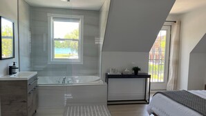 A modern bedroom with a large window, a built-in bathtub, a bedside table, and a bed. - Water view - Perfect location - Modern cottage in Niagara region  (Niagara-on-the-Lake)