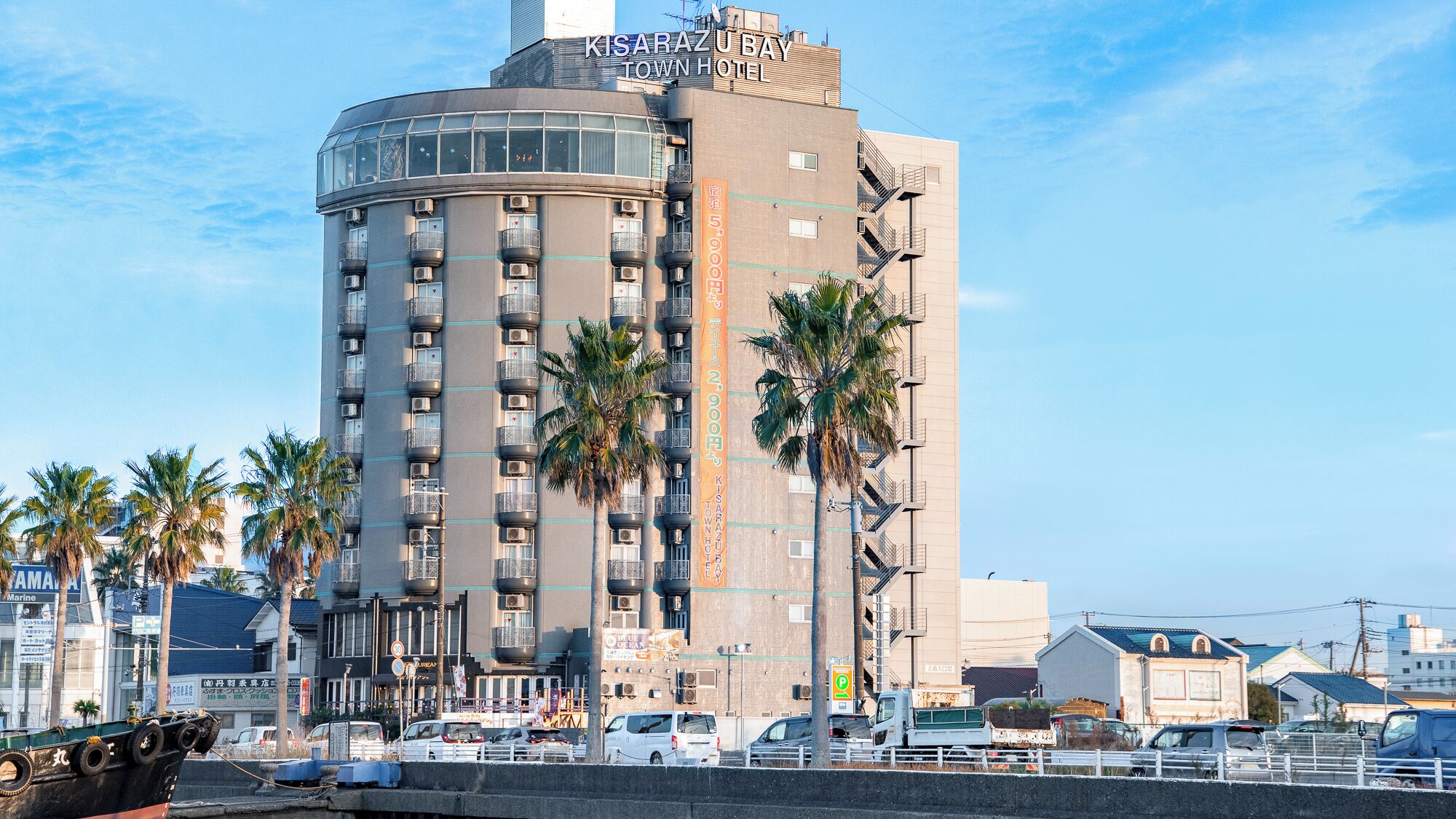 Un hotel alto con fachada curva, varios balcones y palmeras en primer plano.