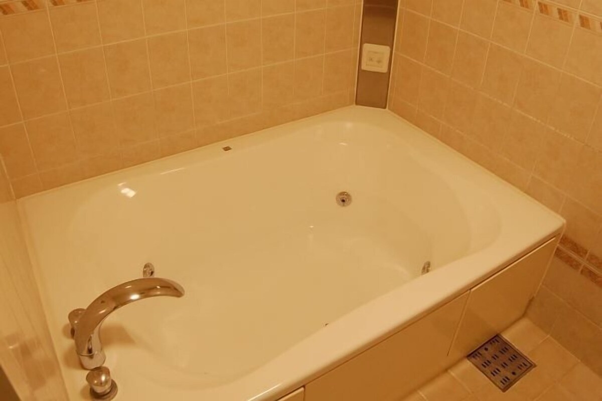 Un baño con una bañera blanca, un grifo cromado y paredes cubiertas de azulejos color beige.
