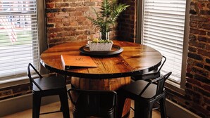 Uma mesa redonda de madeira com quatro cadeiras pretas, um quadro na parede e um vaso com planta sobre a mesa.