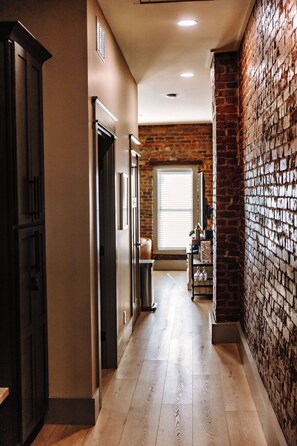 A hallway with a wooden floor, a brick wall, and a door leading to a room. - THE SEEKA SUITE
NEWLY RENOVATED! COZY & MODERN APARTMENT RIGHT ON COURT SQUARE!
 (Bardstown)