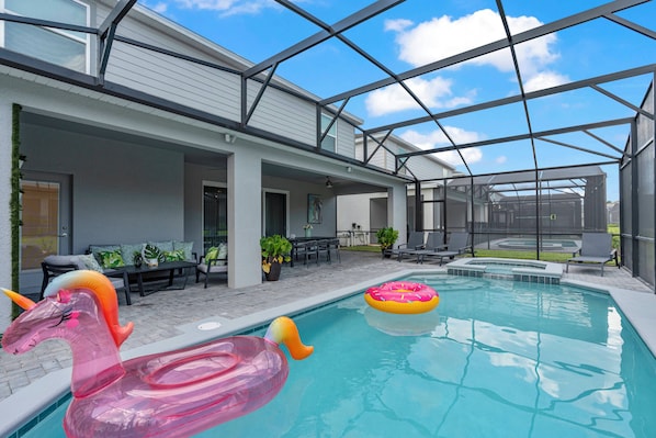 A swimming pool with inflatable unicorn and flamingo floats, surrounded by a covered patio with outdoor furniture and plants.