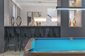 Enjoy our stylish game room with a vibrant turquoise pool table for friendly competition, sleek black bar stools at a chic counter, and modern lighting that creates a warm atmosphere for evening gatherings.
