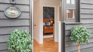 A wooden cottage entrance with a sign reading 'Piglet Cottage,' a wooden door, a window, and two potted plants. - UK47693 - Piglet Cottage (Wimbish)