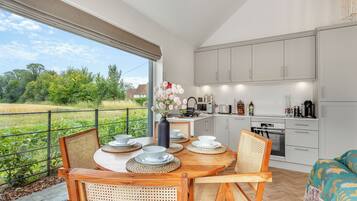 A modern kitchen with white cabinets, a dining area with a round table and chairs, and a view of a green field through large windows.