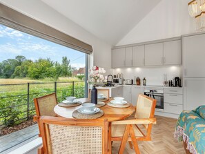 A modern kitchen with white cabinets, a dining area with a round table and chairs, and a view of a green field through large windows.