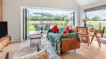 A spacious living area with a sofa, chairs, a TV, and a view of a garden through large windows.