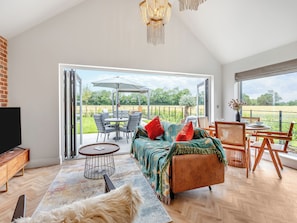 A spacious living area with a sofa, chairs, a TV, and a view of a garden through large windows.