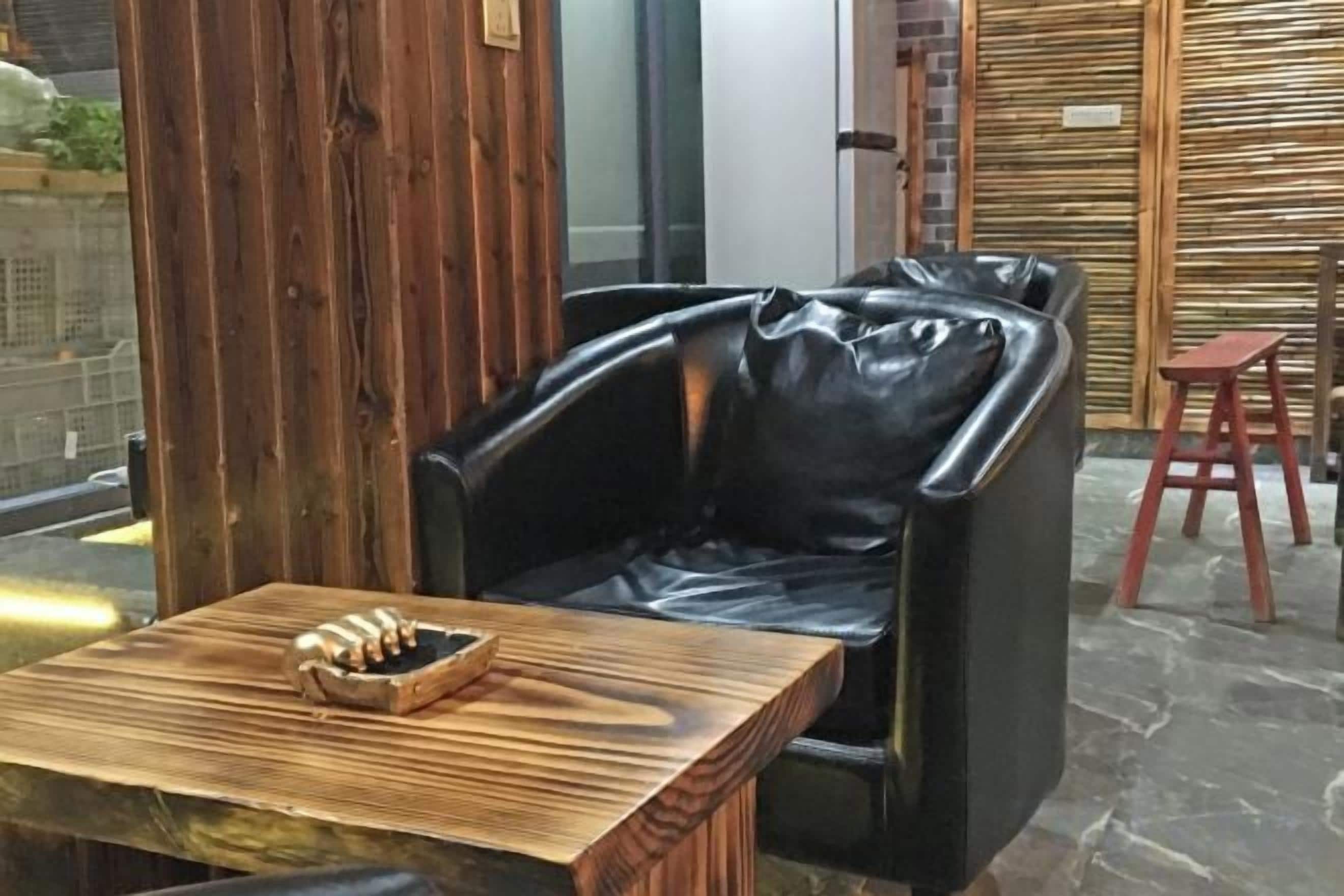 Un área de estar con un sillón de cuero negro, una mesa de madera con un cuenco y un taburete rojo.