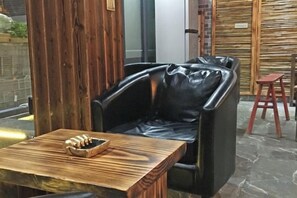 A seating area with a black leather chair, a wooden table with a bowl, and a red stool. - Linxi Xiaoyin Homestay (Yunhe)