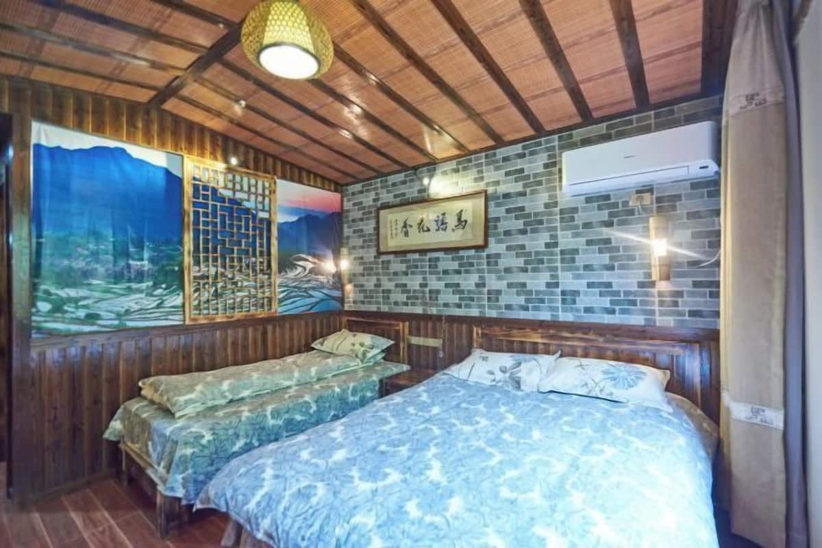 A room with a bed, two smaller beds, a wooden ceiling, a wall-mounted air conditioner, and a framed sign.