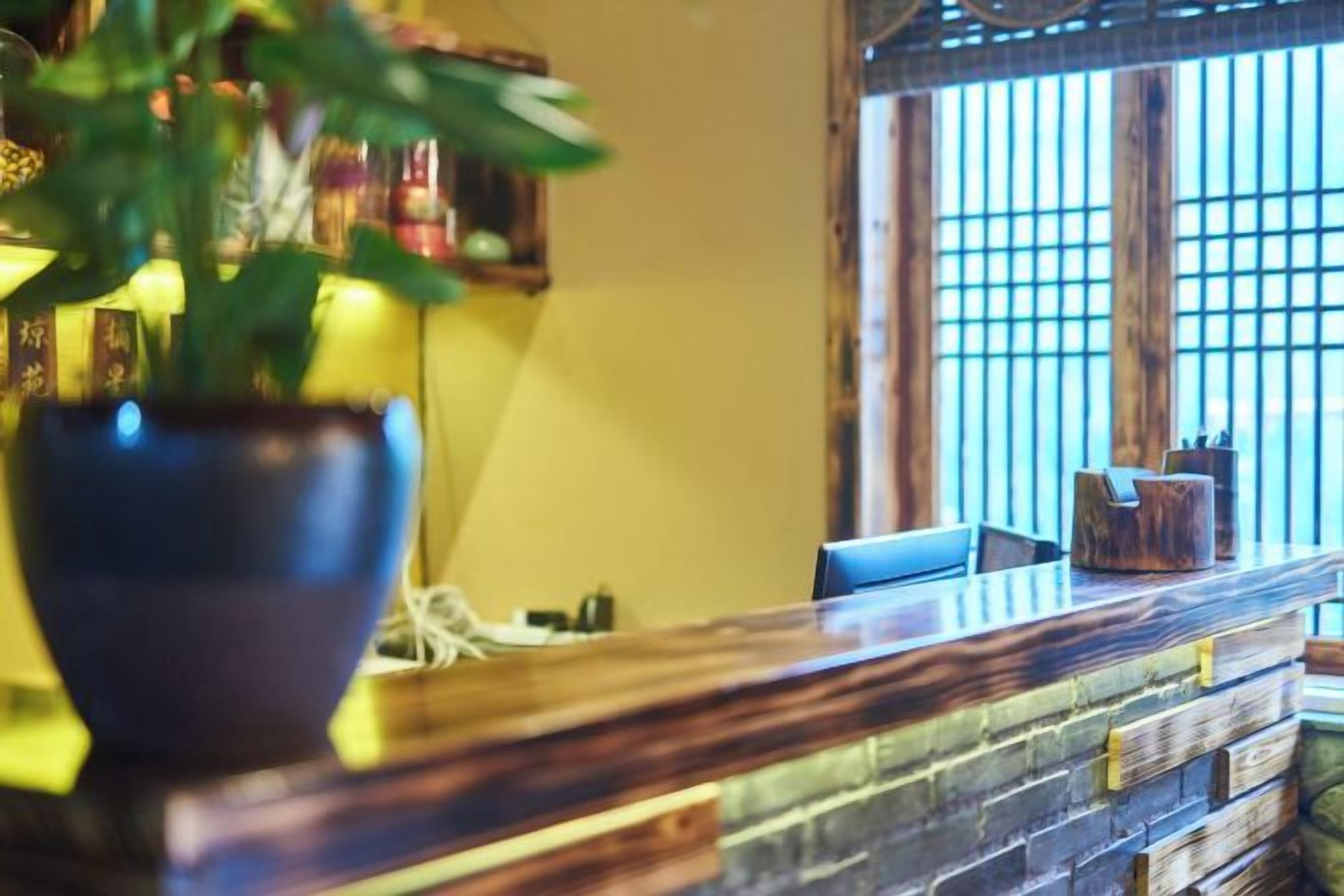 Un mostrador de recepción con una planta en maceta, encimera de madera y una ventana con persianas verticales.