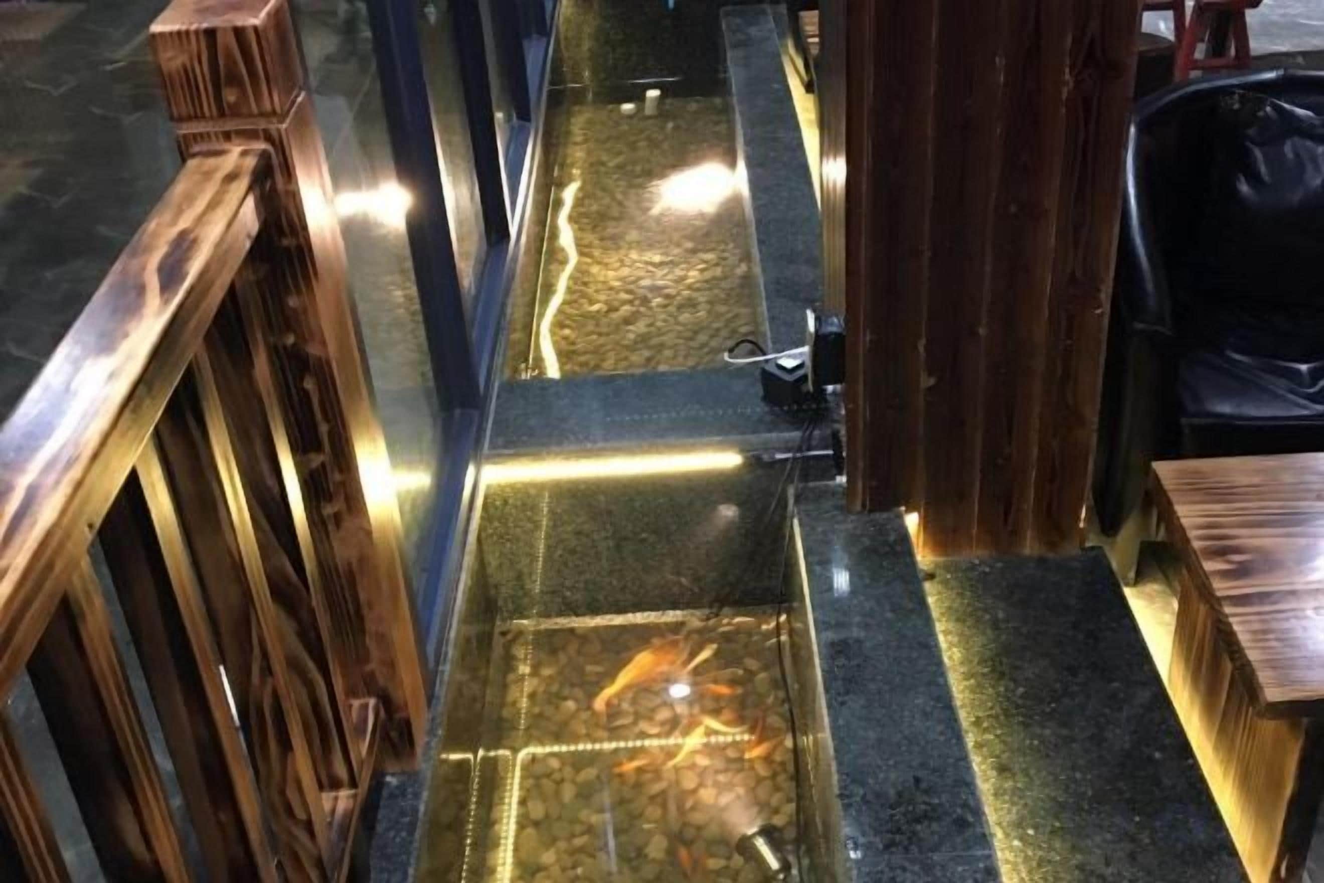 A wooden railing, a fish pond, and a black object on a table.