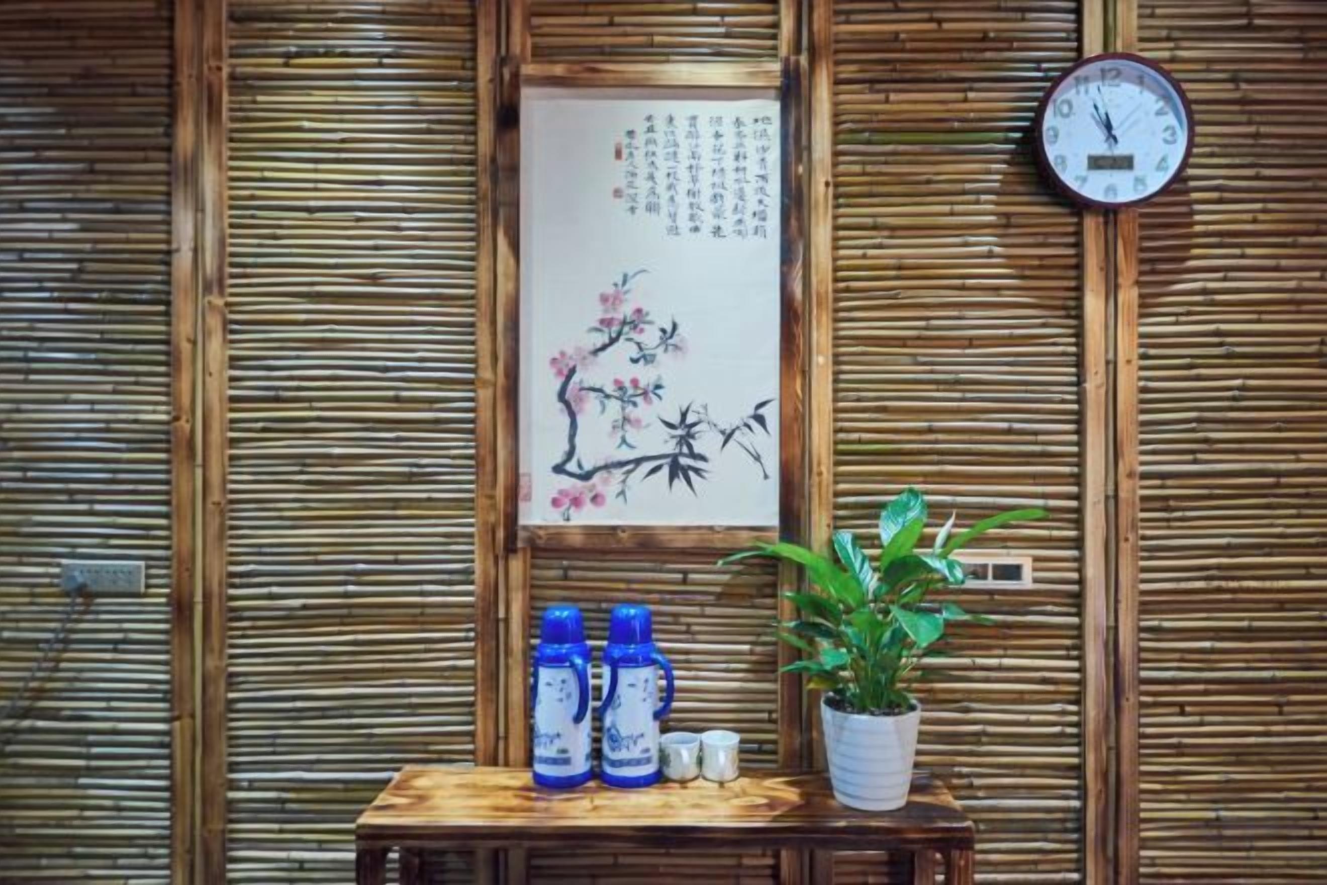 A wooden wall with a framed artwork, a clock, and a small table with bottles and a plant.
